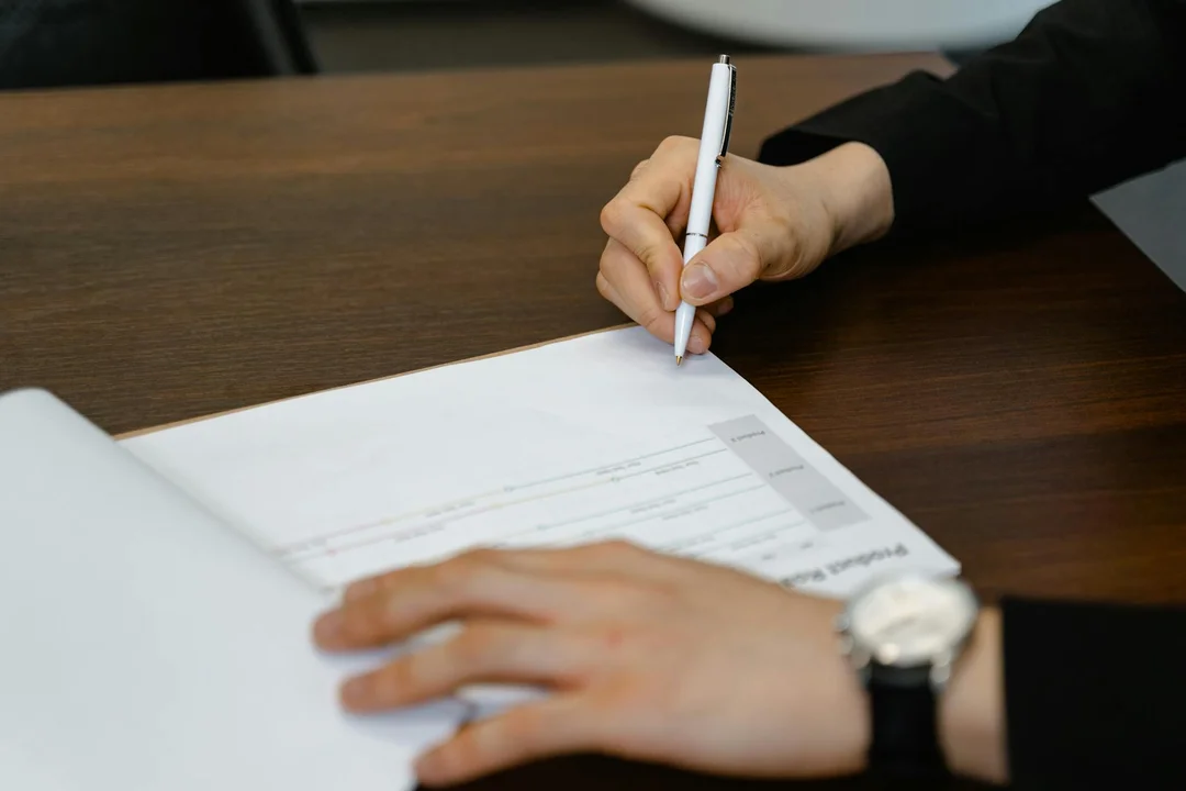 Close-up of hands signing documents on a desk, related to renewing HOA covenants.