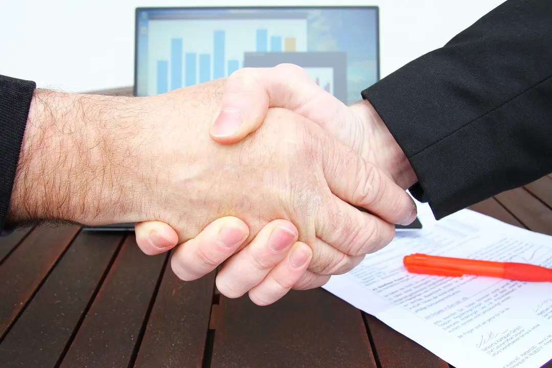 Handshake between two professionals over a contract on a desk, with a laptop in the background, illustrating enforcement and compliance in HOA governance