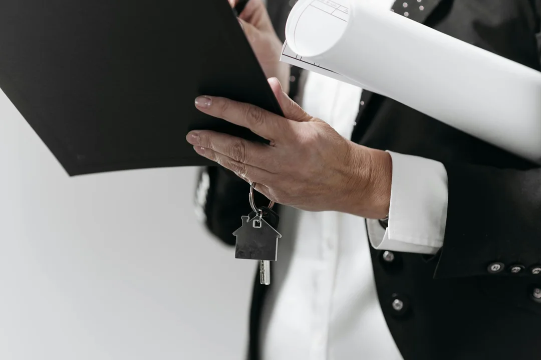 Professional in a suit holding a clipboard and a rolled document, with a house-shaped keychain, symbolizing HOA management and the need to verify data.