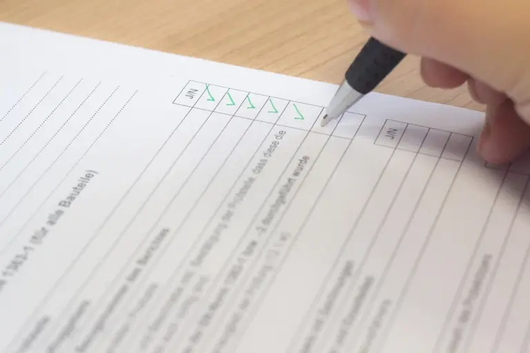Close-up of a hand holding a pen and checking boxes on a printed checklist.
