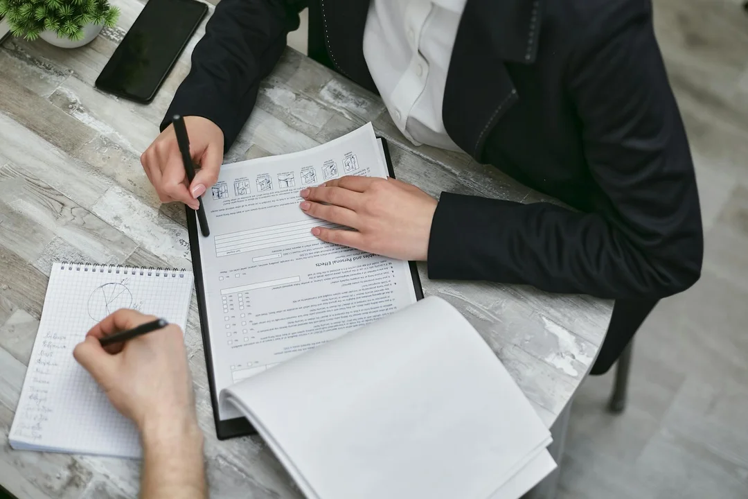 Two professionals in business attire review a document on a clipboard and take notes at a desk, illustrating a fair housing compliance audit for an HOA.
