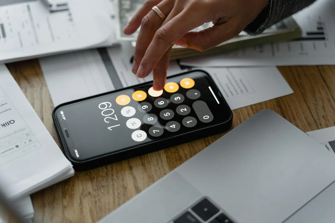 Close-up of a hand using a smartphone calculator with mortgage documents on a wooden table, illustrating budgeting for HOA fees.
