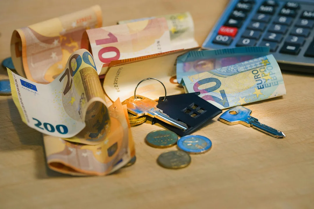 Euro banknotes, coins, keys, and a calculator on a wooden surface.