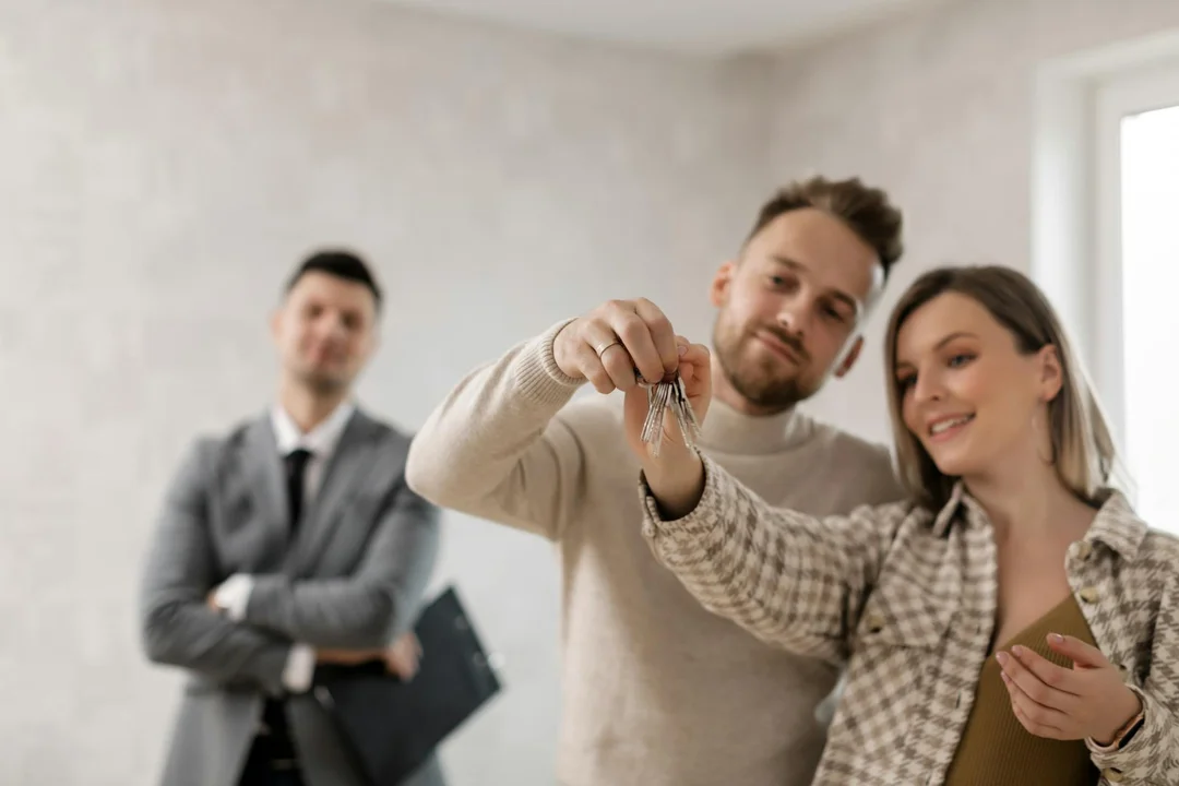Couple receiving house keys from a real estate agent in a modern interior, illustrating HOA-related mortgage discussions.