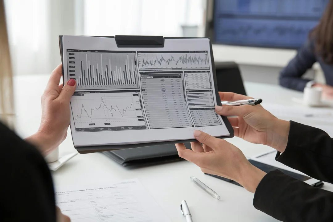 Two professionals examine a clipboard displaying financial charts and spreadsheets during a meeting