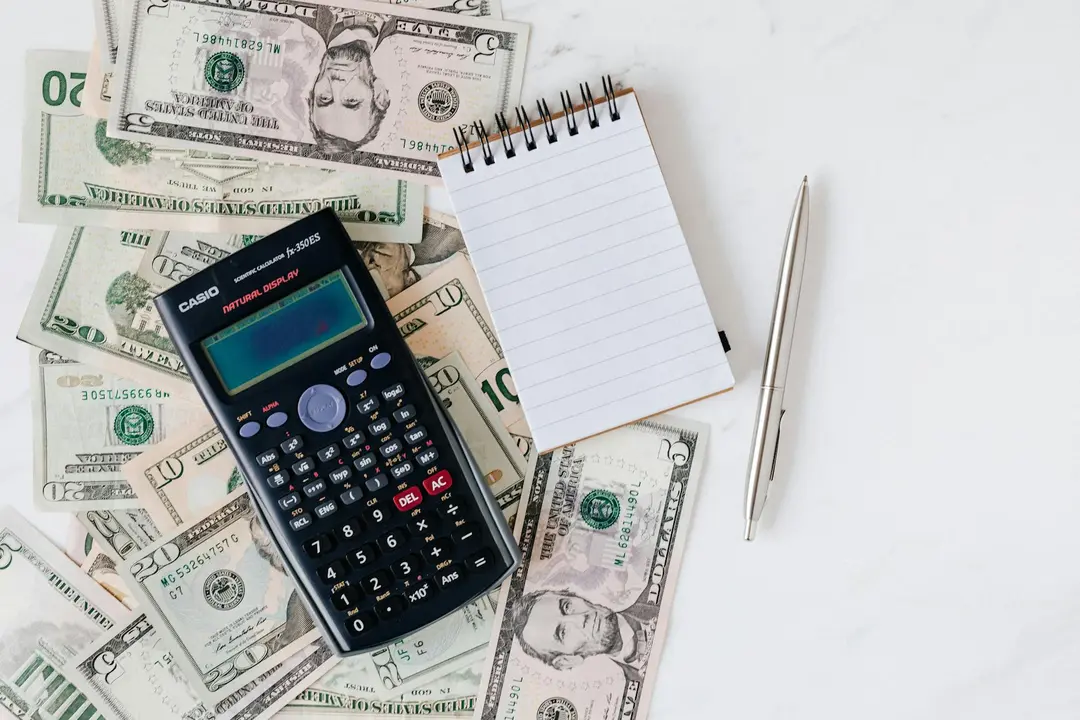 Calculator, notepad, pen, and scattered dollar bills on a white surface, symbolizing streamlined financial reporting and transparency for homeowners associations.