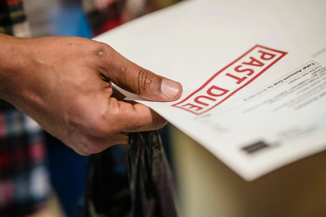 Close-up of a hand holding a document with a large red stamp reading 'PAID DUE'.