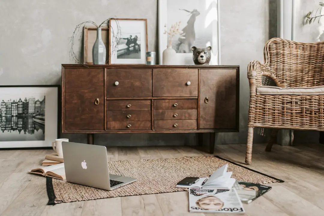 Cozy home workspace featuring a laptop on the floor, scattered documents, and a wooden sideboard, suggesting researching HOA information online.