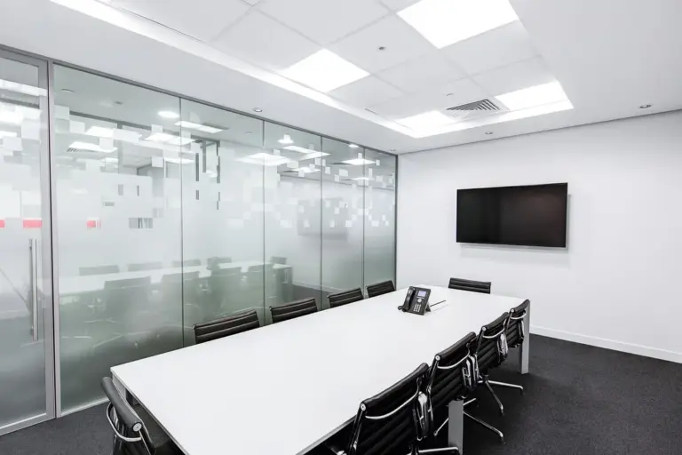 Empty conference room with a long white table, black chairs, glass partition, and a wall-mounted television—evoking a dormant HOA board