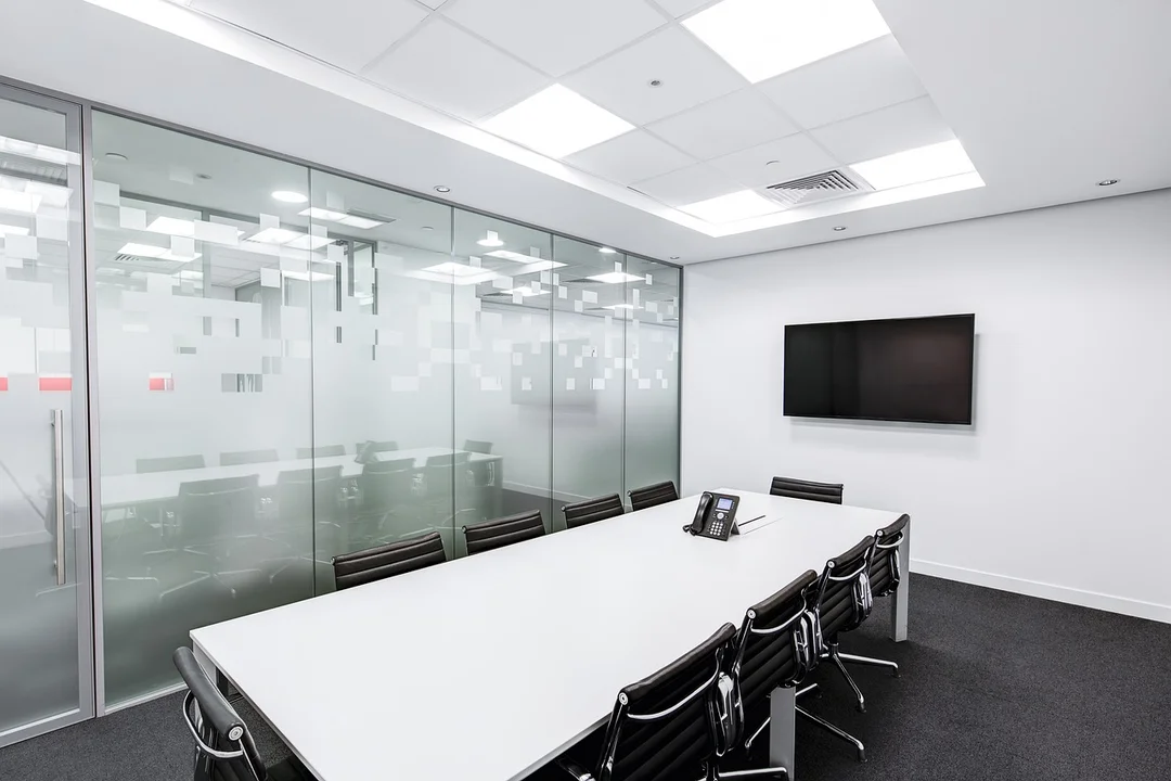 Empty conference room with a long white table, black chairs, glass partition, and a wall-mounted television—evoking a dormant HOA board