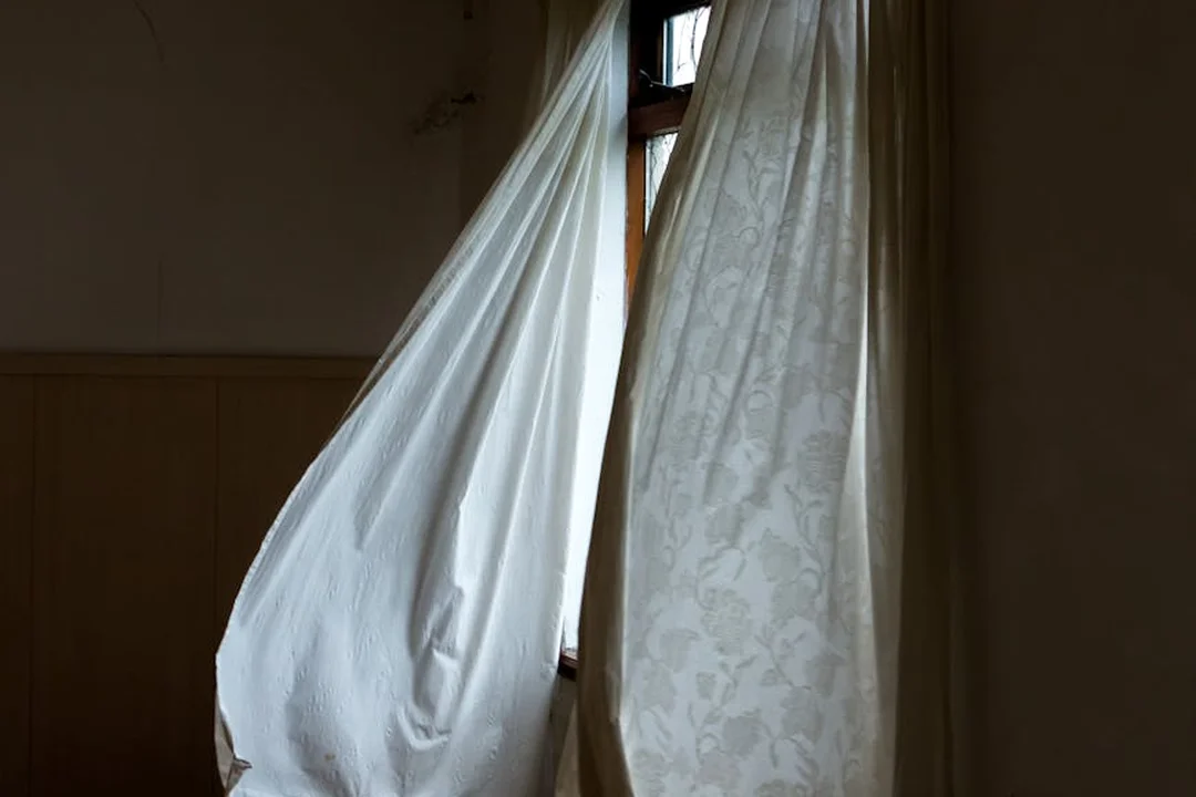 Dim room with white curtains billowing by a window, conveying neglect and inactivity