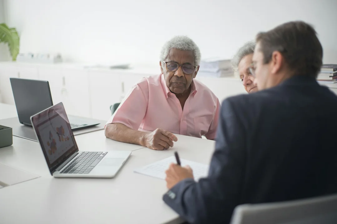 Three professionals sit around a white table in a bright office, reviewing documents and a laptop as they discuss options after a master insurance claim denial.