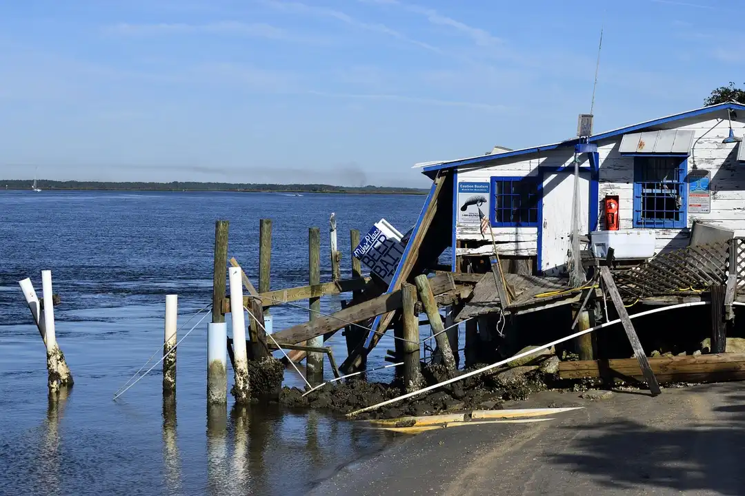 A damaged waterfront house with a collapsed dock along the shore after a storm.