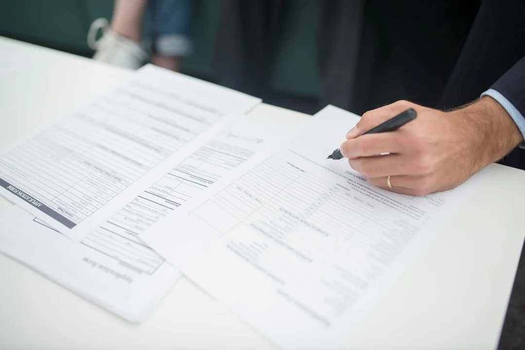 Close-up of a person signing documents on a white desk, representing HOA liability and disaster insurance paperwork