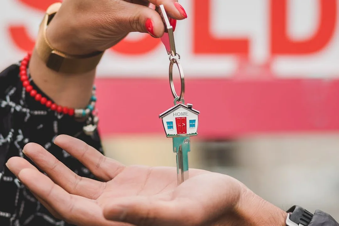 Close-up of a hand receiving a house key with a small home keychain