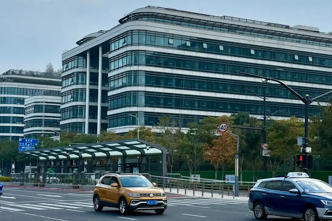 Modern multi-story office building along a busy city street with a bus stop and several cars.