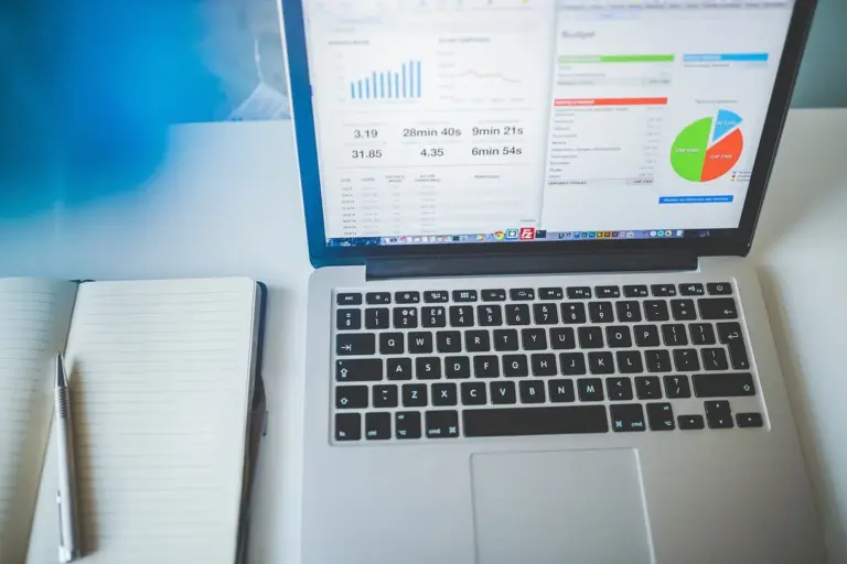 Laptop displaying analytics dashboards on screen, with a notebook and pen beside it.
