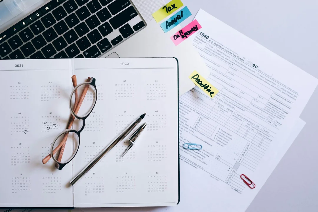 Open calendar on a desk with reading glasses, a pen, and financial documents with color-coded sticky notes