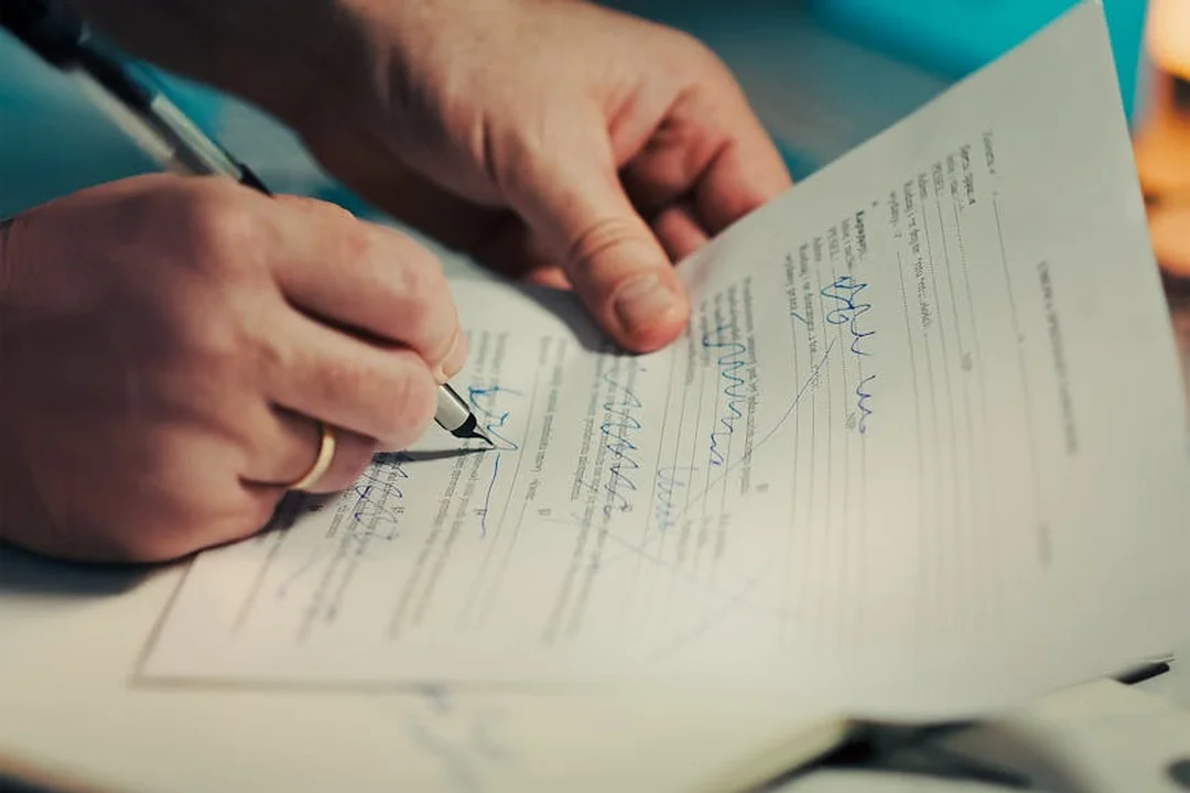 Close-up of hands signing a document with a pen on a desk