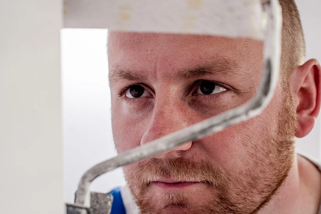 Close-up of a man with a short beard looking intently while holding a paint roller for painting a wall.