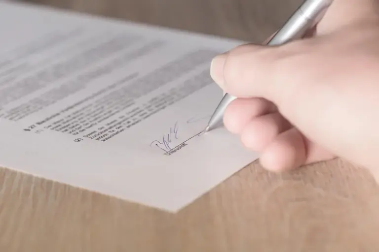 Close-up of a hand signing a document with a pen, representing agreeing to an HOA contract.