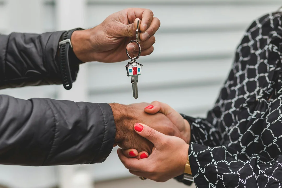 Close-up of two people shaking hands during a real estate closing, with one person handing over house keys.