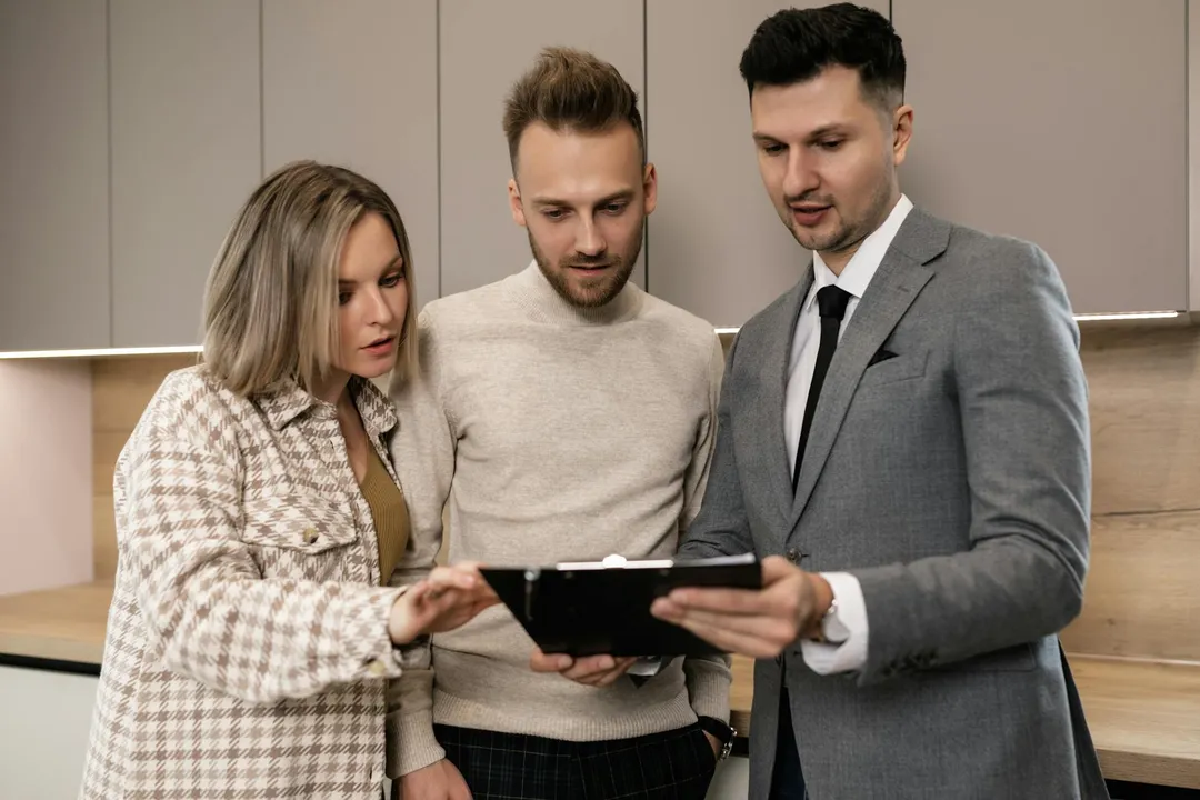 Three adults in a modern kitchen examine a tablet to review HOA rules and possible violations.