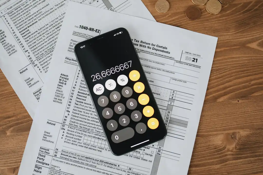 Smartphone displaying a calculator app over tax forms and documents on a wooden desk, illustrating financial planning needed to dissolve an HOA.