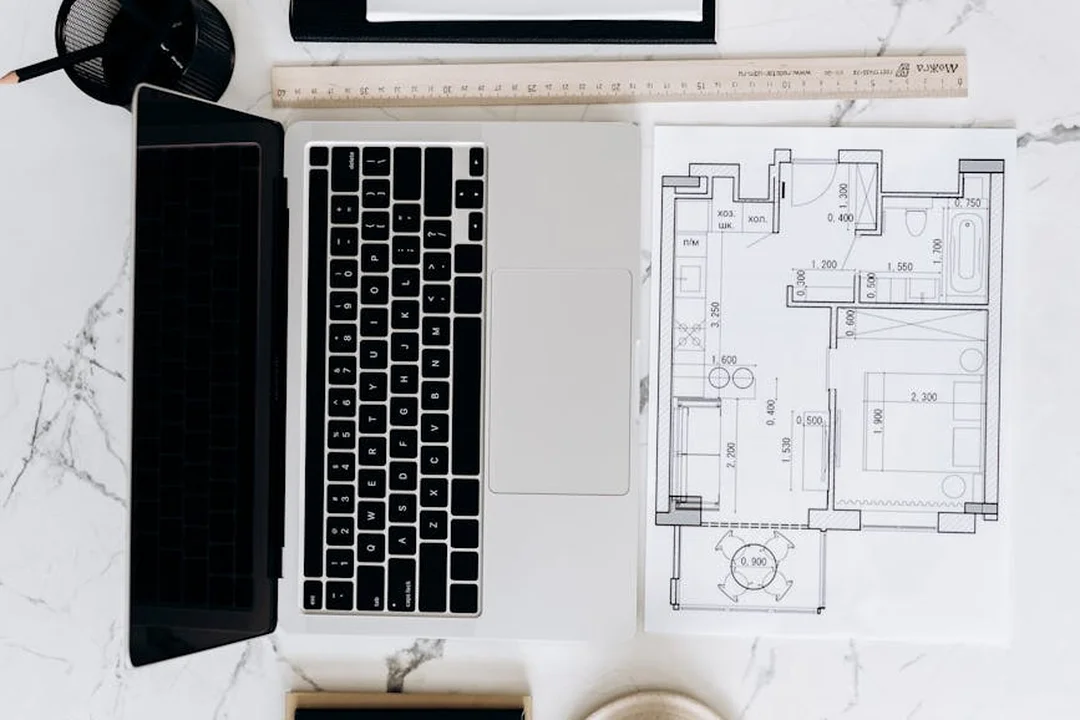 Top-down view of a workstation with a laptop, architectural blueprint, ruler, and coffee cup, illustrating organized planning for HOA architectural requests.