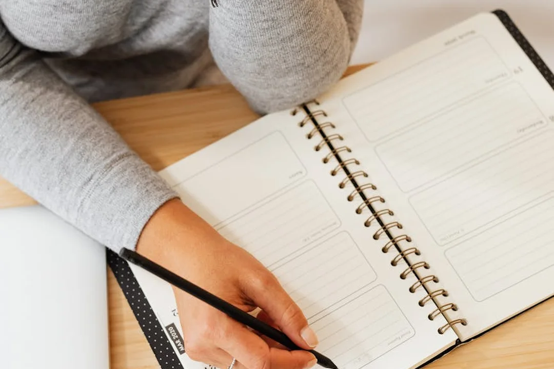 Close-up of a hand writing in a planner or notebook, emphasizing planning and scheduling for HOA communication.