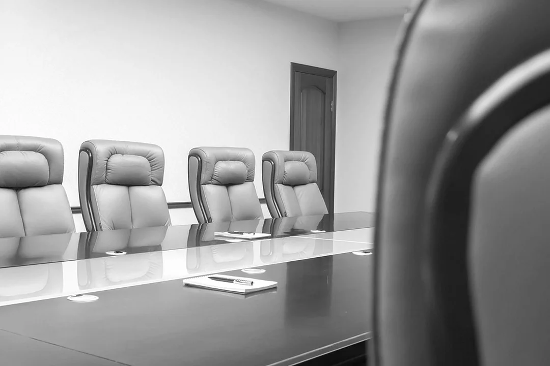 Empty HOA boardroom with a long, polished table and high-back chairs arranged for a meeting, in black-and-white.