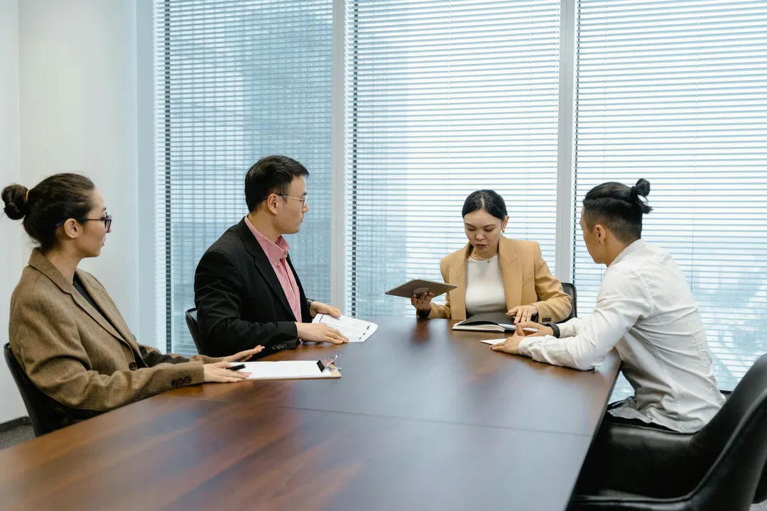 Four professionals sit around a conference table during an HOA board meeting, reviewing documents.