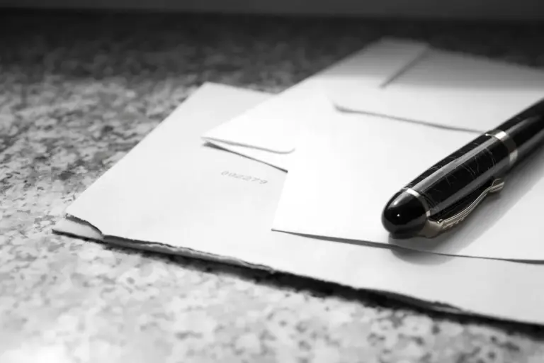 Black-and-white photo of envelopes and a pen on a textured surface, suggesting submitting a resignation letter to an HOA board.