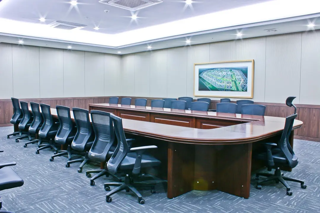 Empty HOA boardroom with a large curved wooden table surrounded by black swivel chairs; a framed map hangs on the wall.