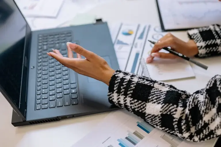 Person typing on a laptop at a desk with documents and charts, illustrating reviewing HOA bylaws and covenants