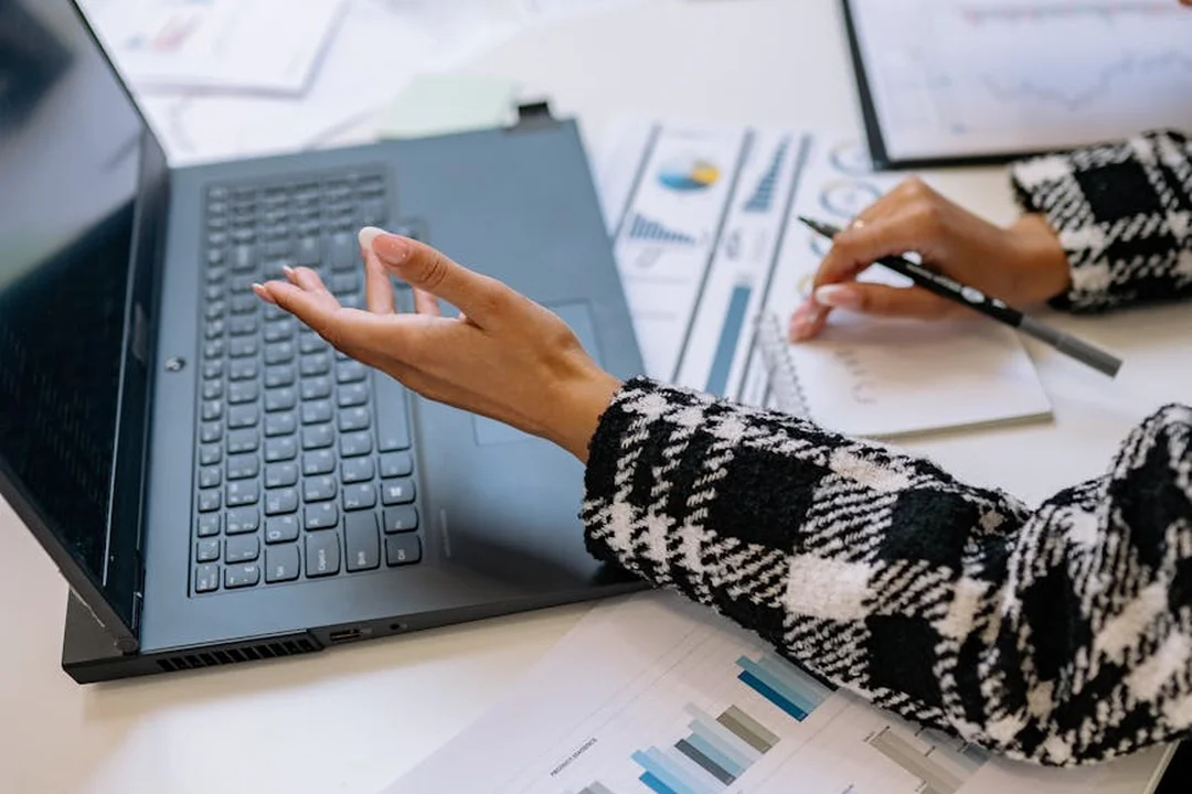 Person typing on a laptop at a desk with documents and charts, illustrating reviewing HOA bylaws and covenants