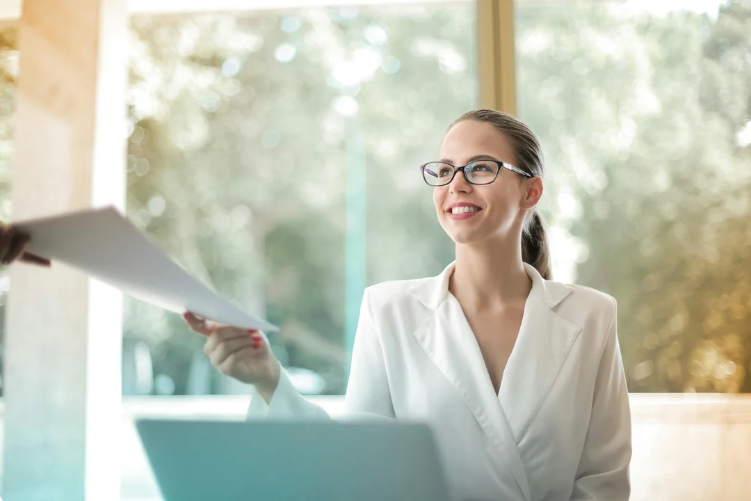 Smiling professional in a white blazer presents documents, symbolizing guidance on homeowners' rights and dispute resolution under HOA covenants, conditions, and restrictions.