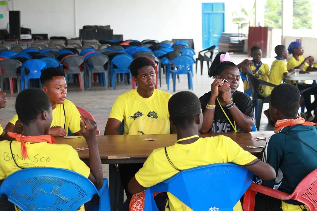 Group of residents seated at tables in an HOA community center, with blue plastic chairs and bright yellow shirts, engaged in conversation.
