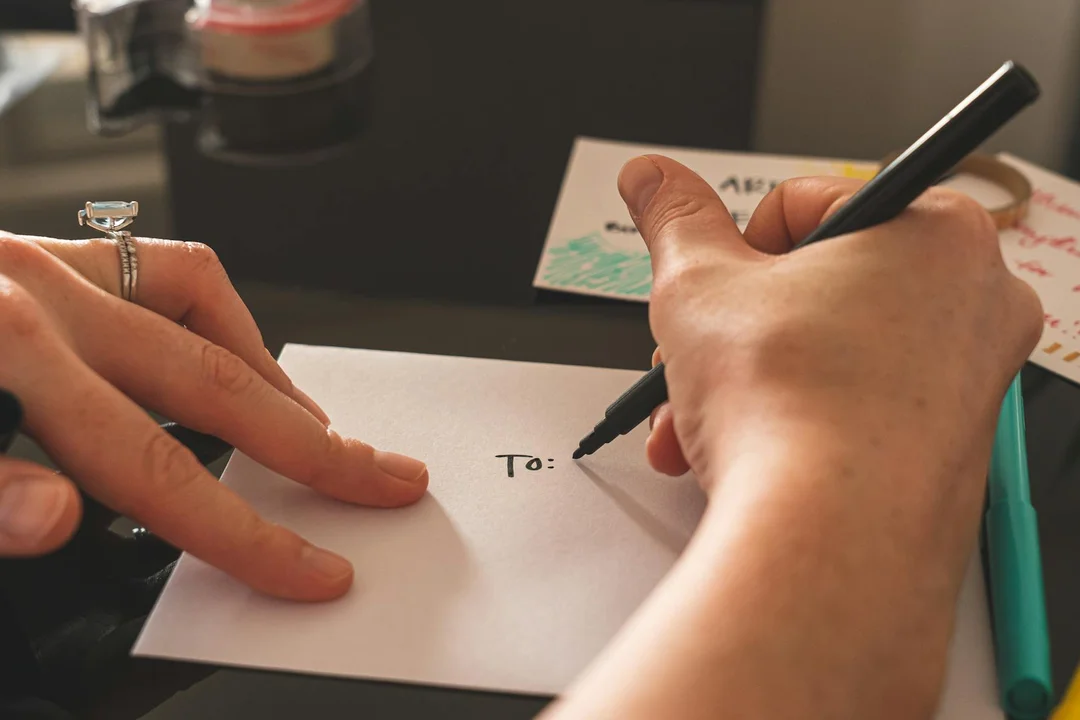 Close-up of hands writing on a small white card with 'To:' visible.