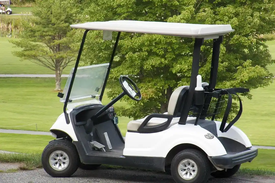 White golf cart parked on a path in a green HOA community with trees and grass in the background.
