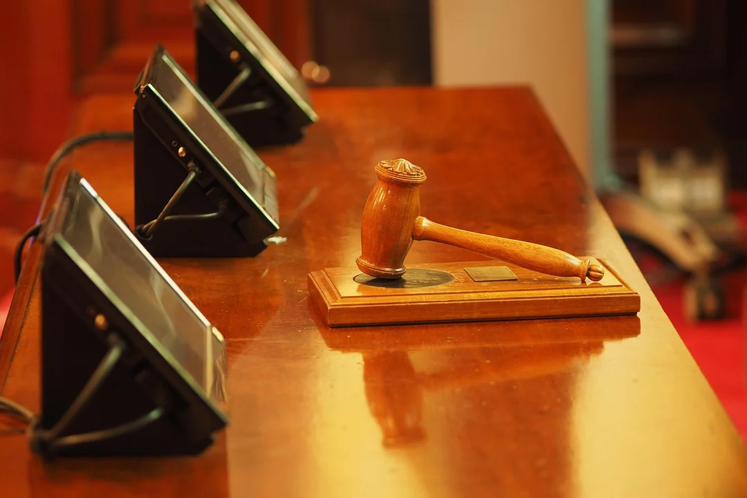 Gavel resting on a polished wooden desk with several conference telephones in the background, suggesting a formal decision-making setting.