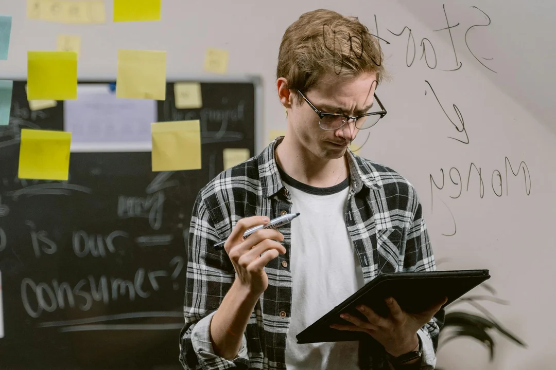 A person wearing a plaid shirt and glasses stands at a whiteboard with sticky notes, holding a tablet and pen, illustrating careful planning and professional preparation for addressing an HOA dispute.
