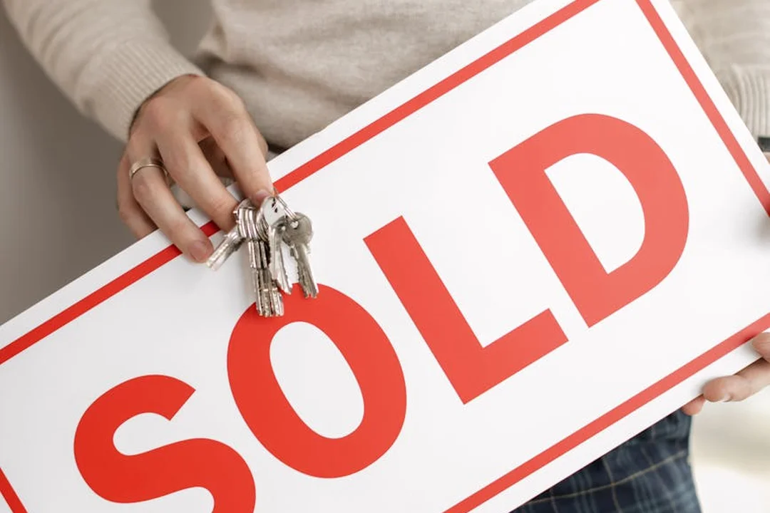 Close-up of a hand holding a large red 'SOLD' sign with a set of keys attached, representing asset distribution after HOA dissolution