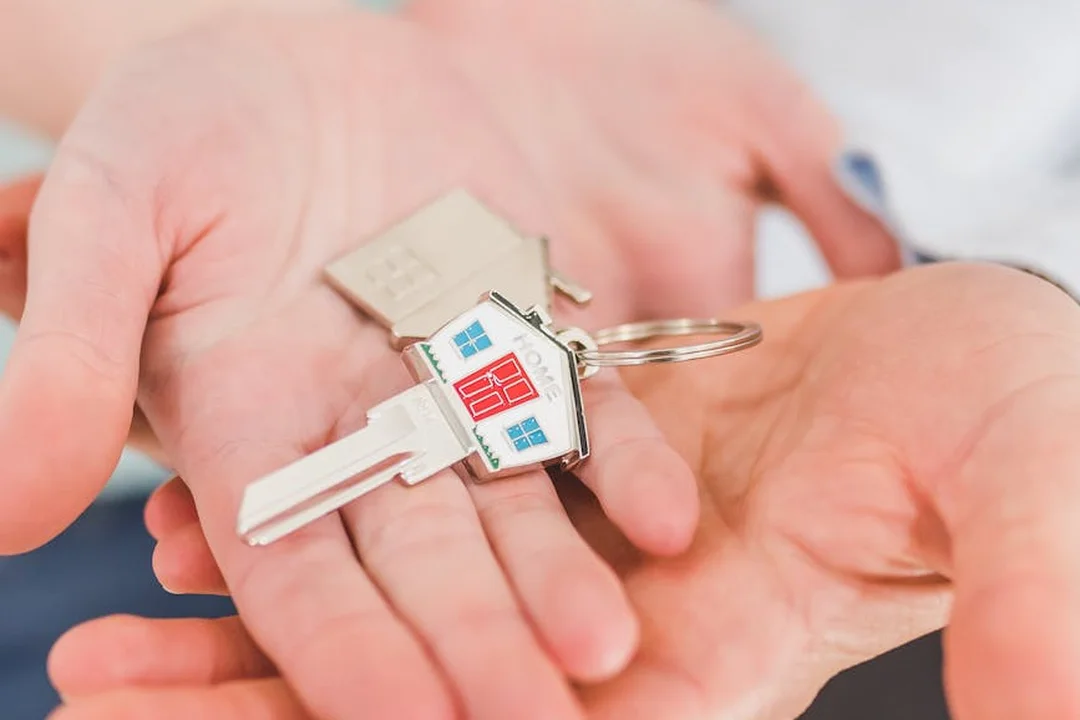 A pair of hands holding house keys with a small house-shaped keychain
