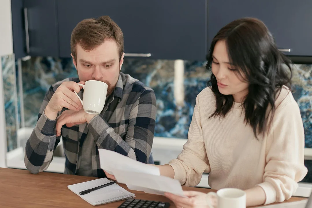 A man and a woman sit at a table reviewing documents, with a notebook and calculator, discussing HOA dissolution procedures.