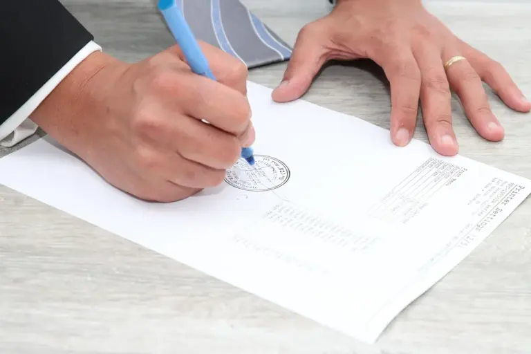 Close-up of hands signing a document with a blue pen and a seal