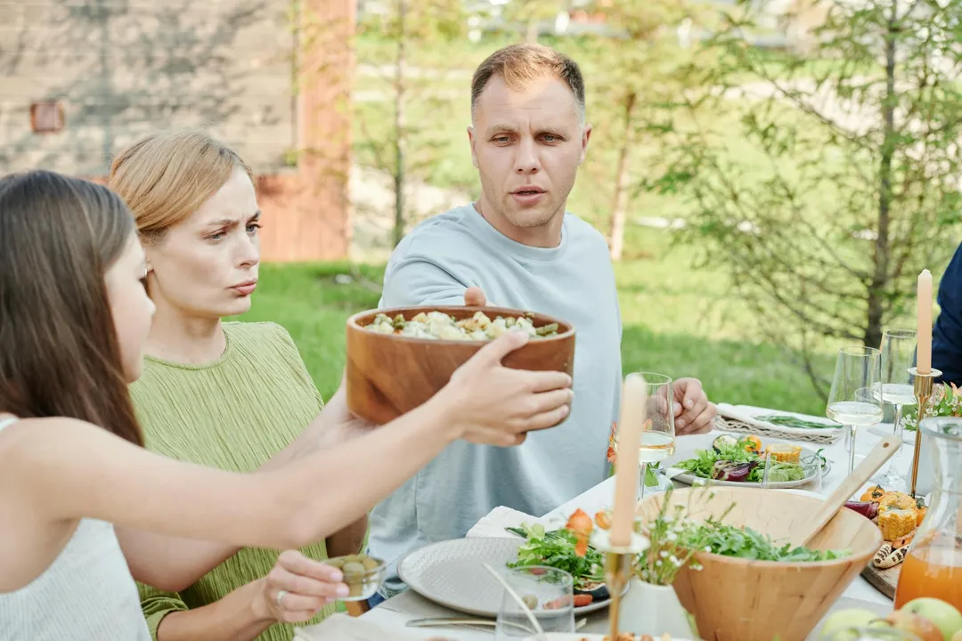 A tense outdoor dinner scene where a man reaches for a bowl as others look upset, illustrating a dispute over HOA rules affecting non-members.