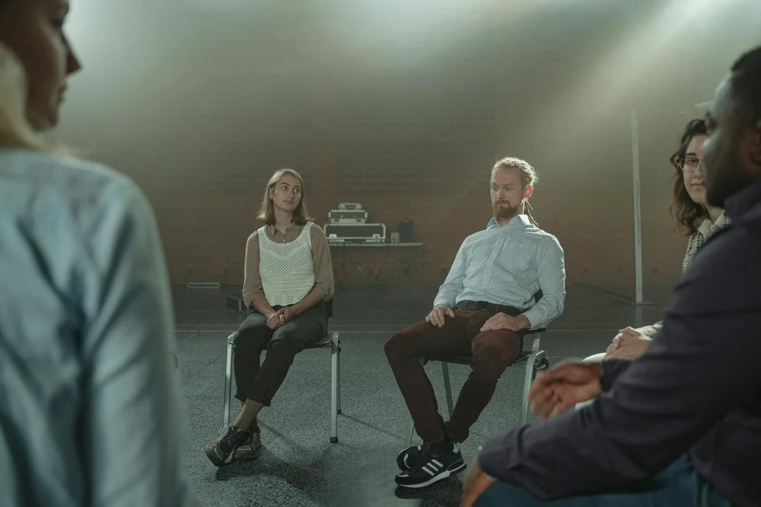 Small group of homeowners seated in a circle in a dim meeting room, engaged in discussion, with a projector on a shelf in the background.