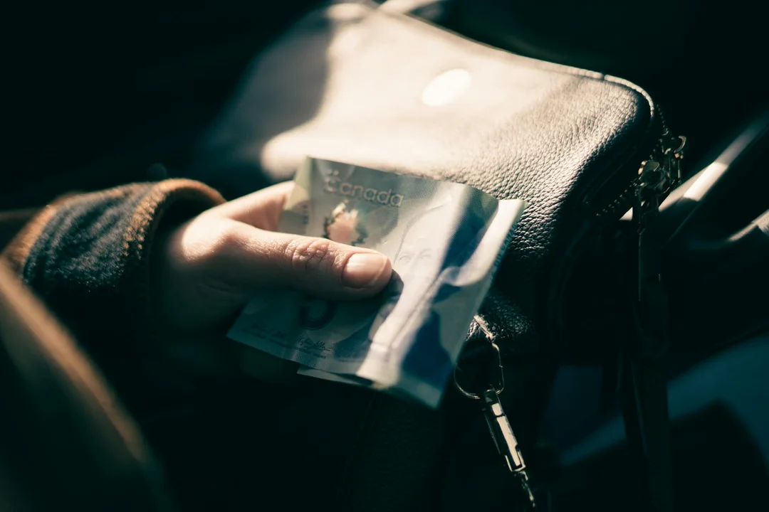 Close-up of a hand holding cash near a purse, illustrating budgeting for HOA costs