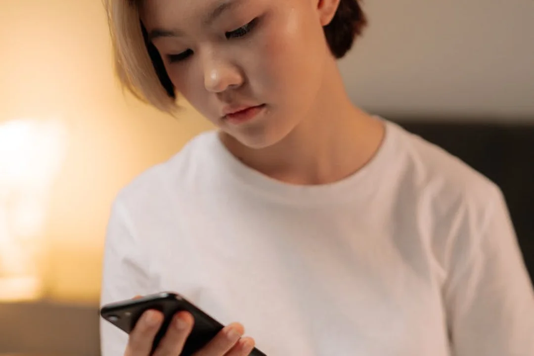 Person in a white shirt looks at a smartphone indoors, symbolizing digital tools for financial management and transparency in land-lease communities.
